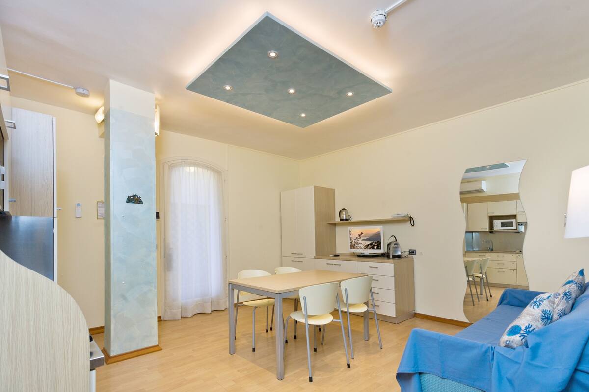 A compact living space with a dining area, kitchenette, and a sofa with a patterned cushion.