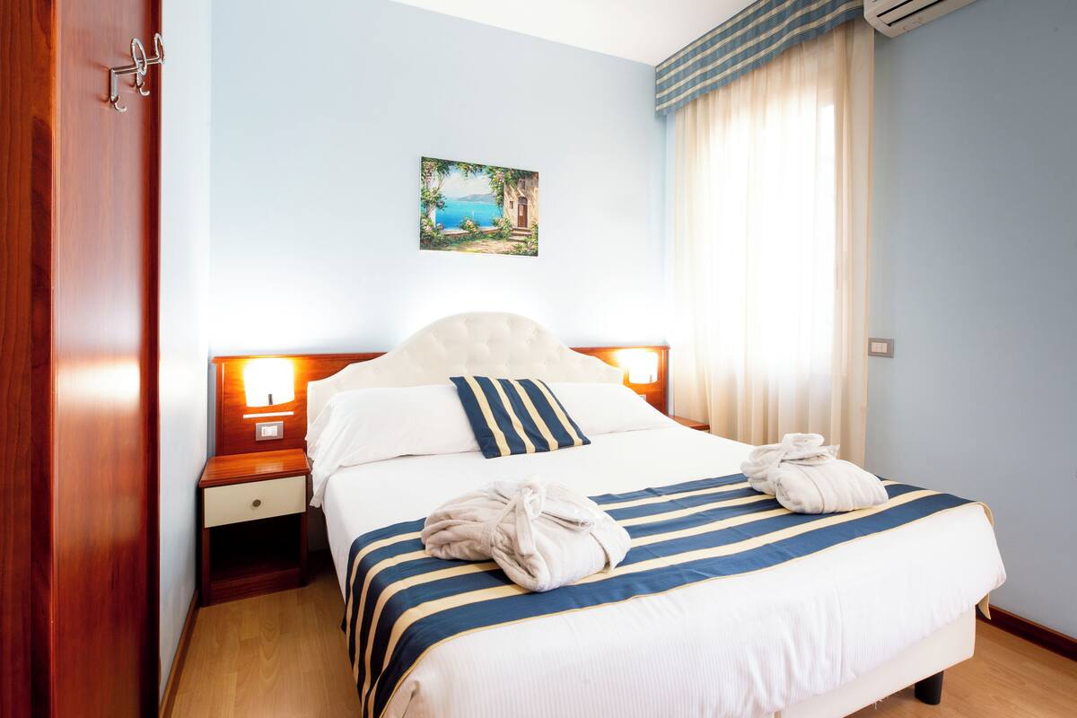 A neatly made bed with striped bedding, a bedside lamp, and a painting on the wall.
