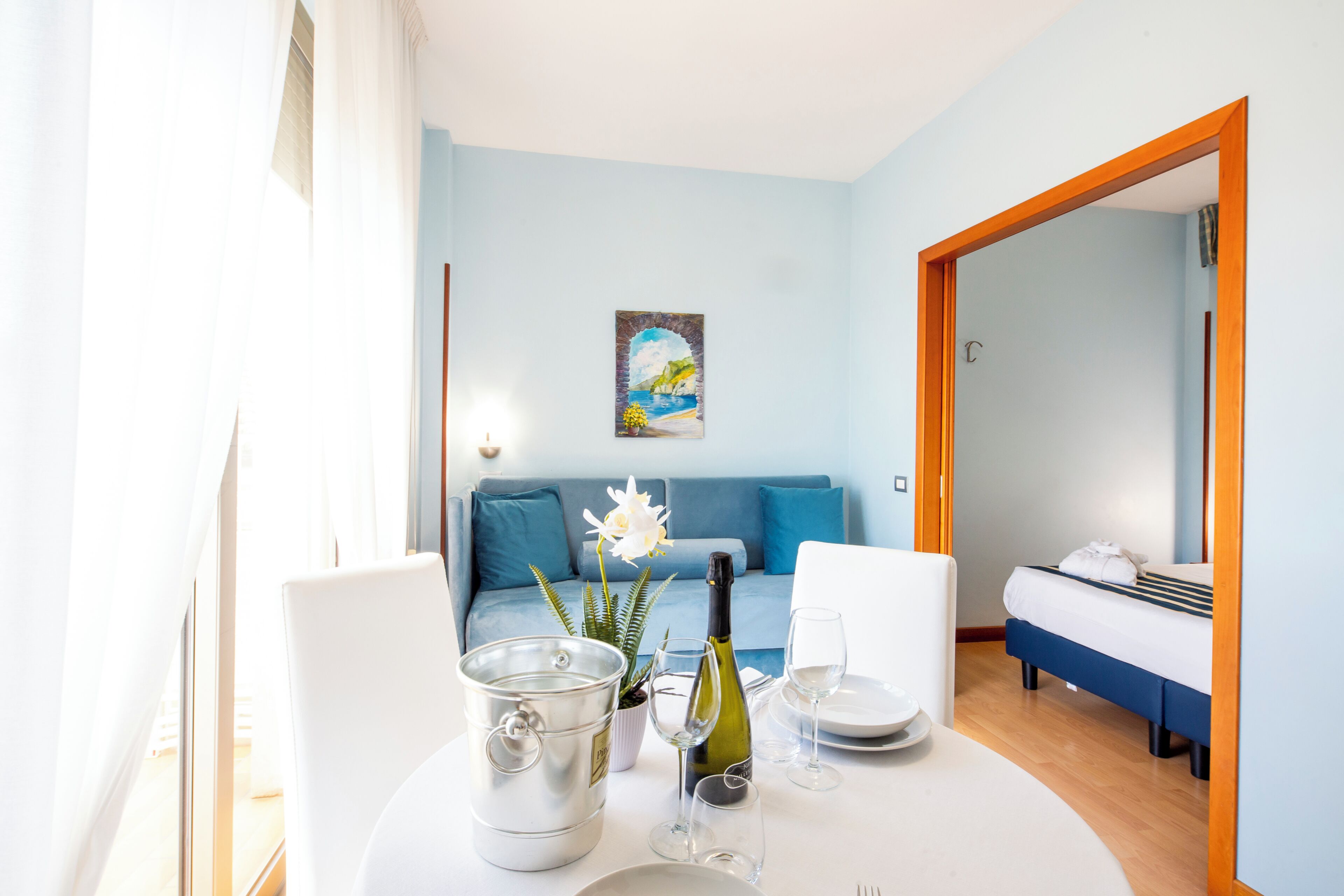 Une pièce comprenant une table à manger dressée pour deux personnes, un lit, un canapé et un tableau accroché au mur.
