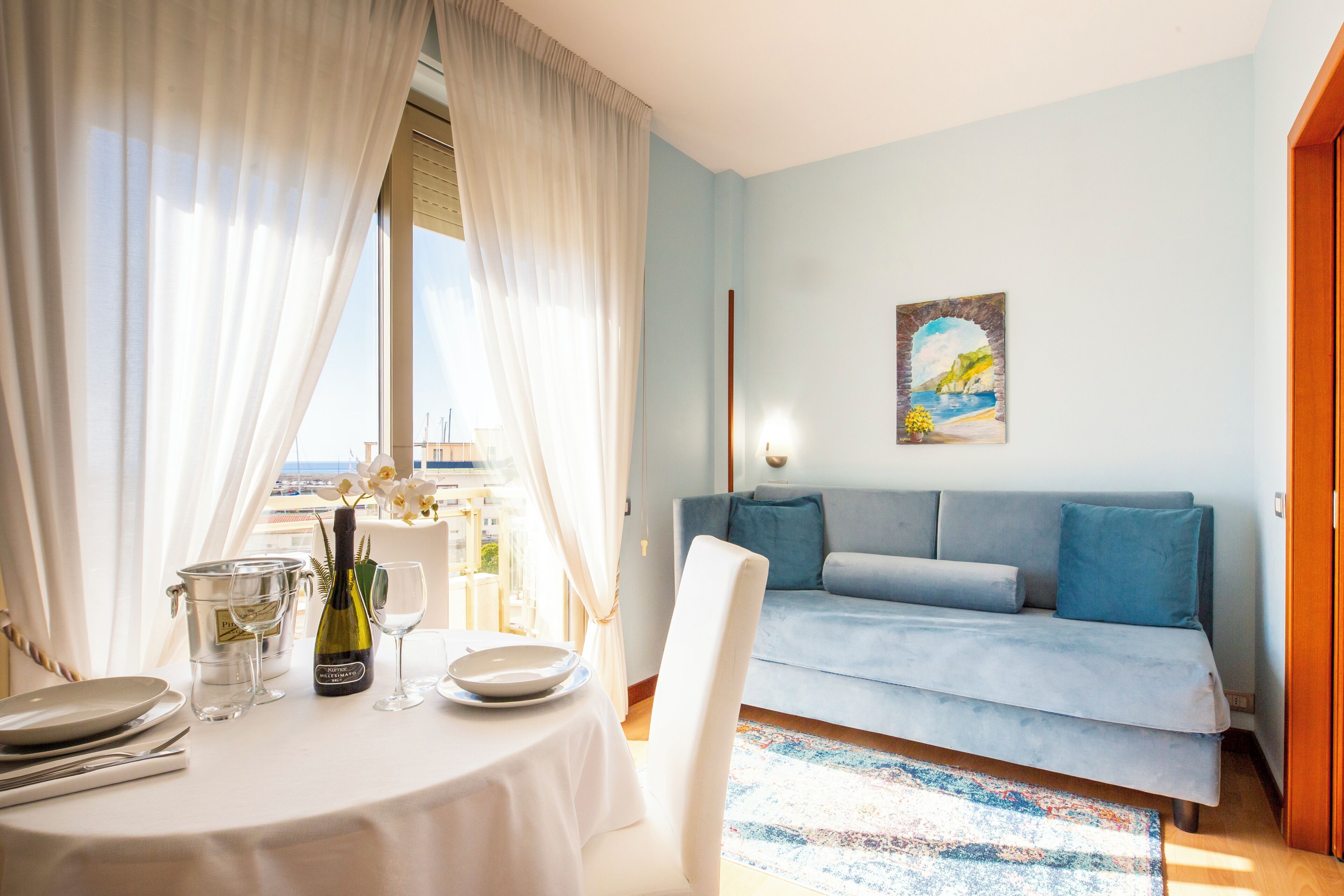 Una habitación con una mesa de comedor preparada para dos personas, un sofá y un cuadro en la pared.