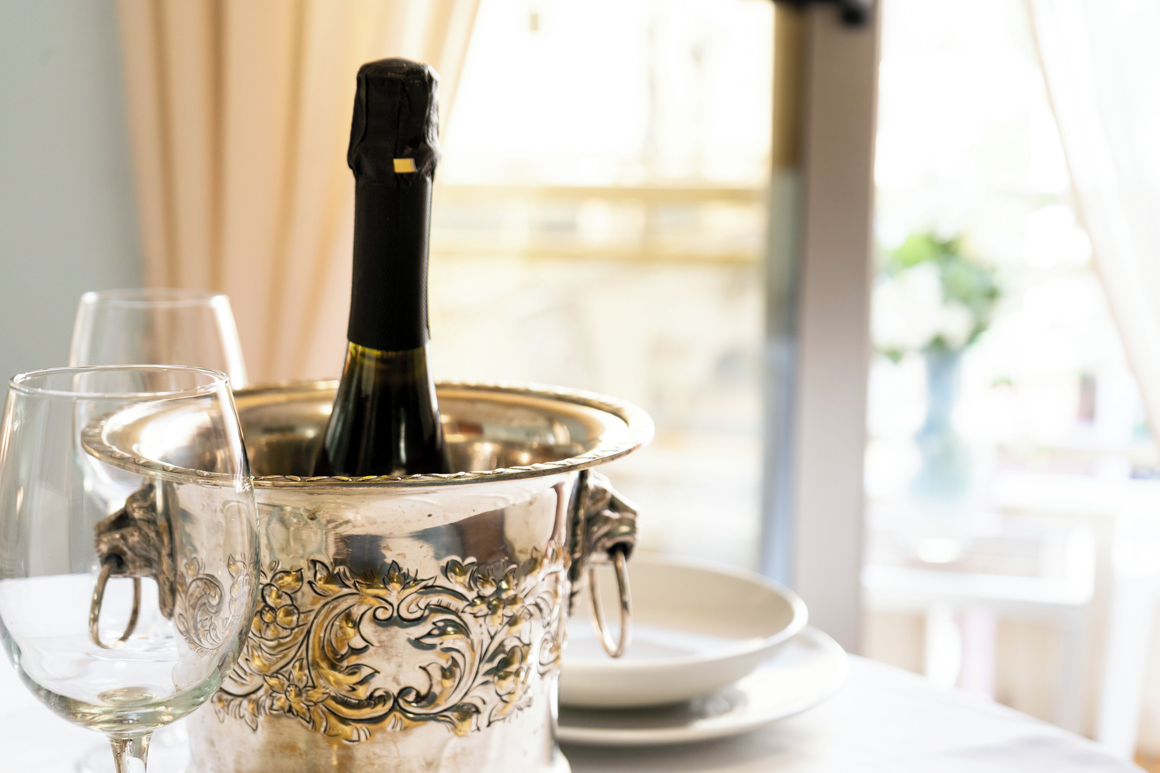A silver decanter with a bottle of wine, a wine glass, and a white plate on a table.