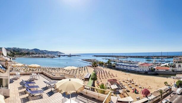 Un hotel frente al mar con terraza con vistas a la playa y al puerto deportivo.