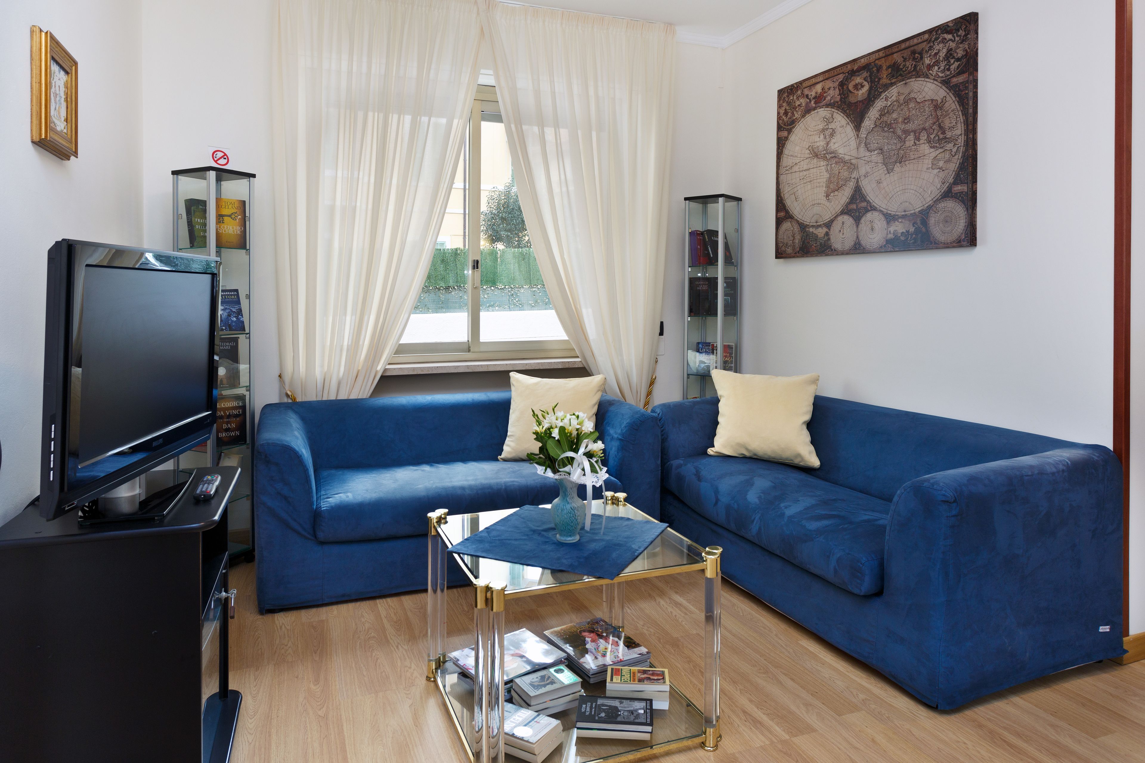 Een woonkamer met een blauwe bank, een glazen salontafel, een televisietoestel en een boekenkast.