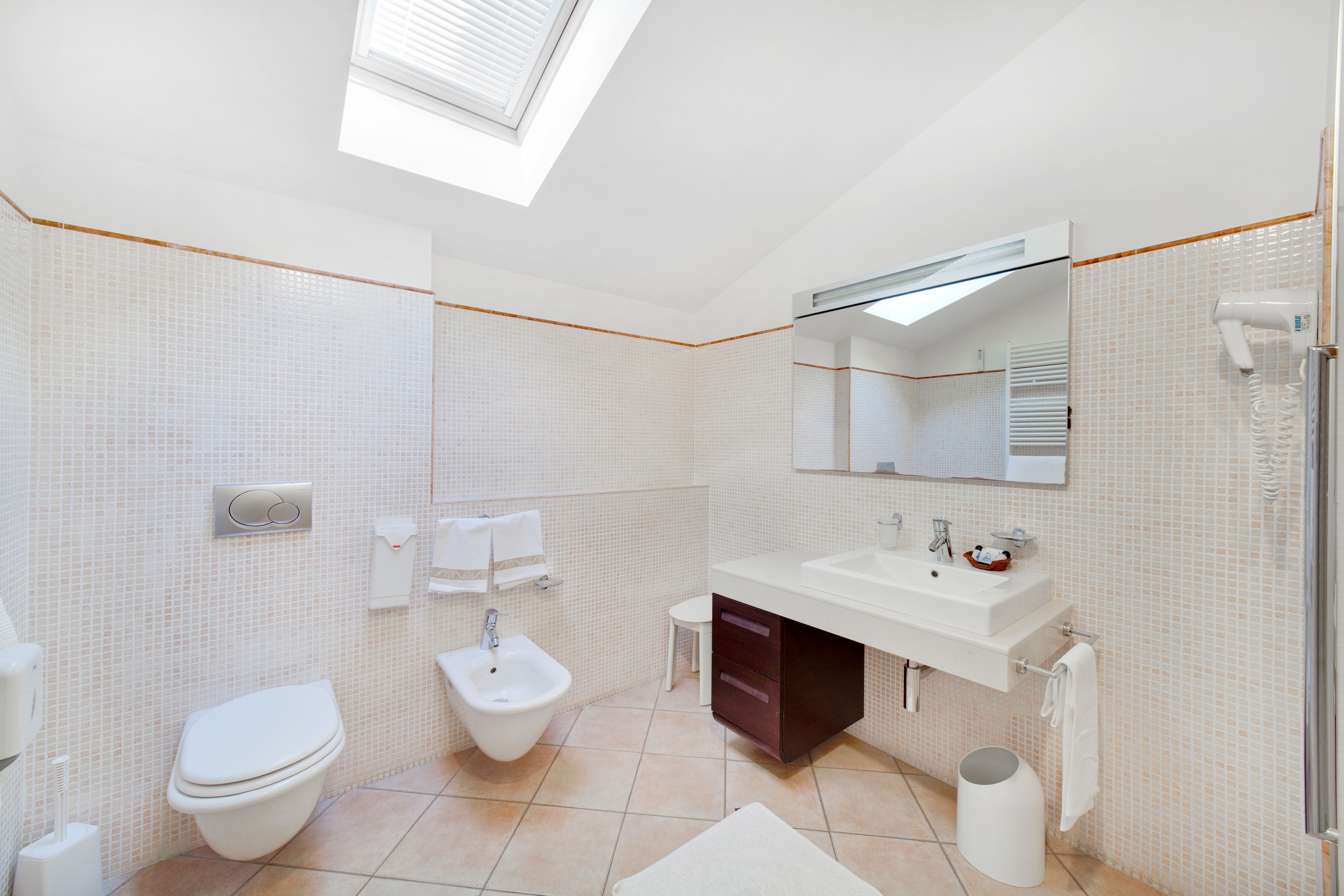 Un baño moderno con tragaluz, un bidé, inodoro, lavabo y espejo.
