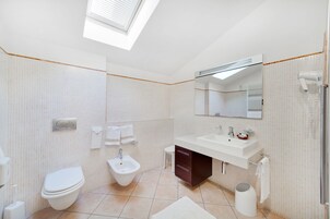 Un baño moderno con tragaluz, un bidé, inodoro, lavabo y espejo.
