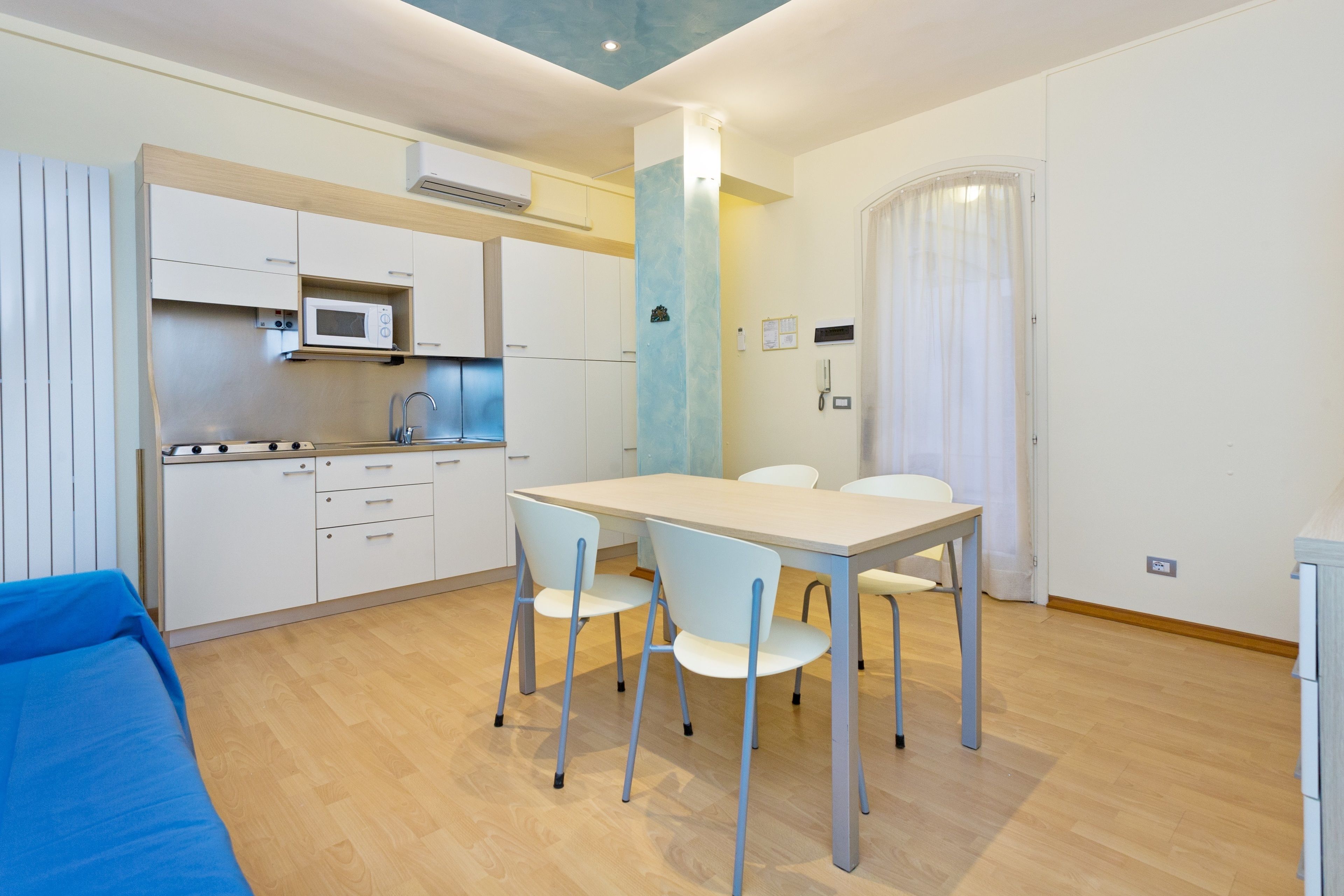 A compact kitchen with white cabinets, a microwave, and a sink. There is a dining table with four chairs.