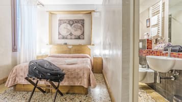 Ein Schlafzimmer mit Bett, Koffer auf einem Hocker, einer Wandgestaltung mit einer Landkarte und einem Badezimmer mit Waschbecken und Spiegel.