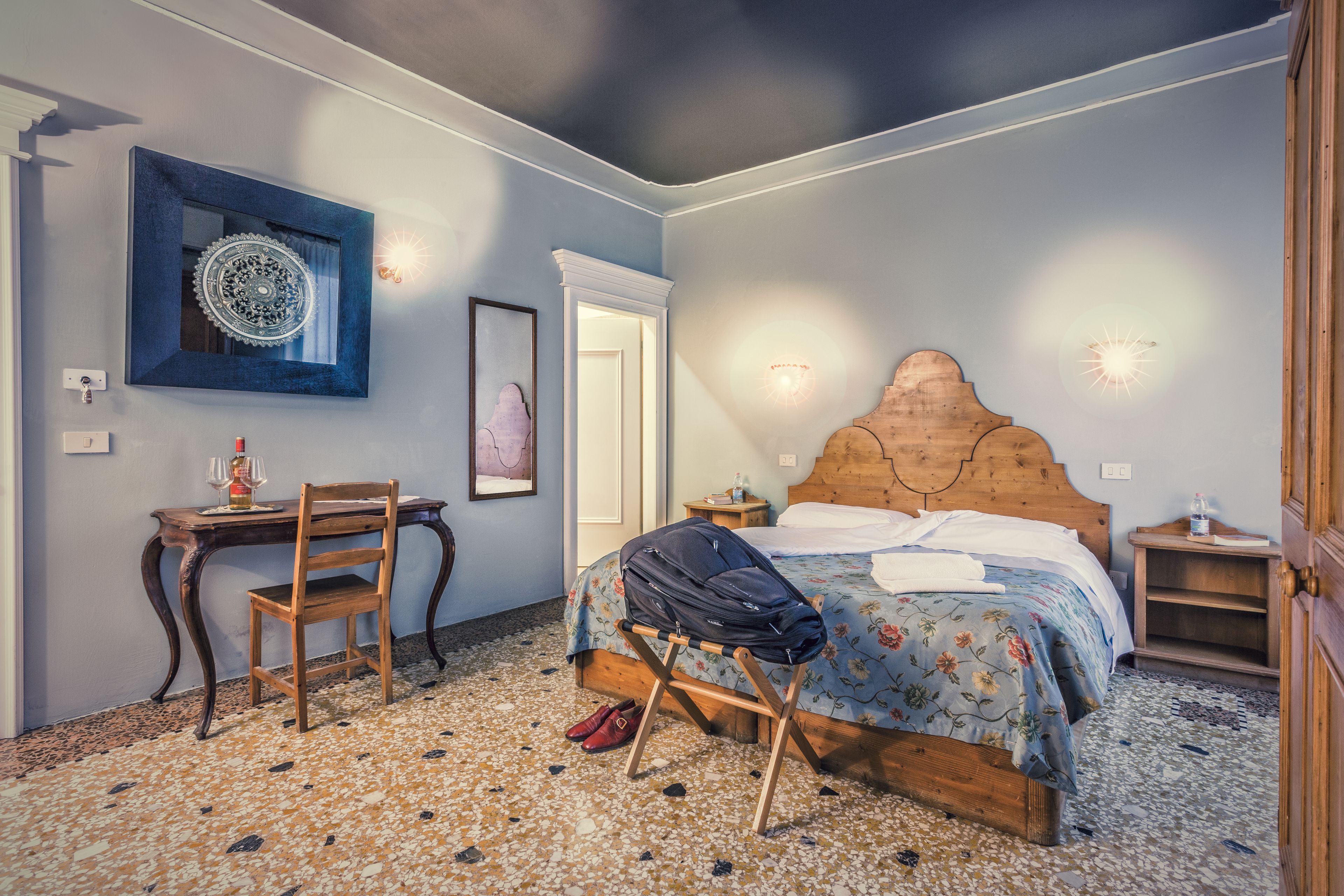 A bedroom with a wooden bed, a desk with a chair, a mirror, and a patterned floor.