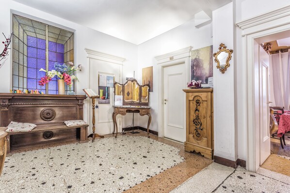 A room with a wooden bench, a mirror, a door with a number, and a window with a stained glass design. - Locanda ai Bareteri (Venice)