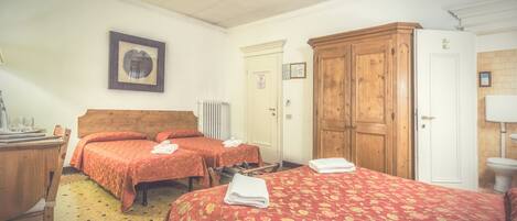 A hotel room with two beds, a wooden wardrobe, a radiator, and a framed picture on the wall.