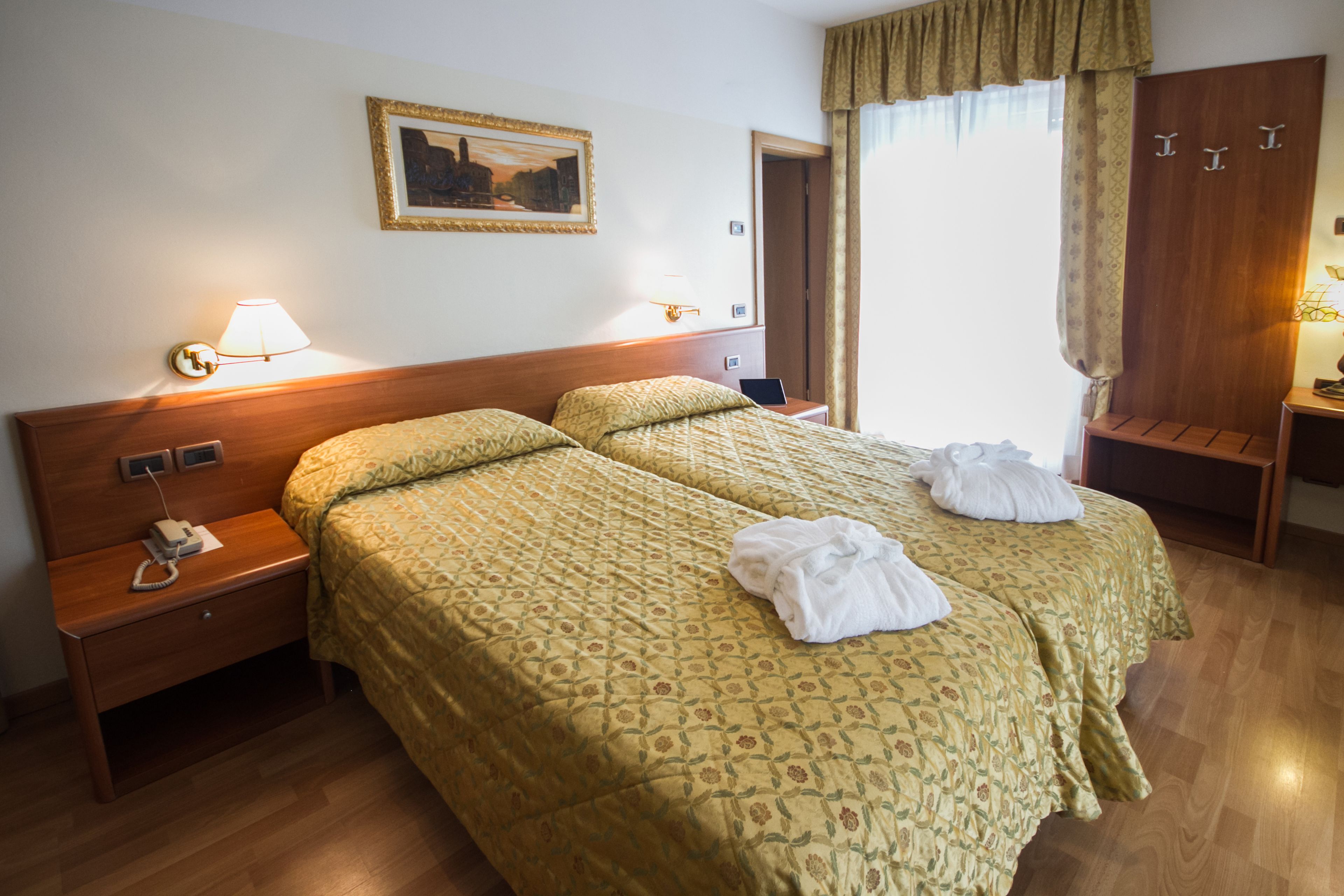 Une chambre d’hôtel avec deux lits, une tête de lit en bois, un tableau au mur et un bureau avec une lampe.