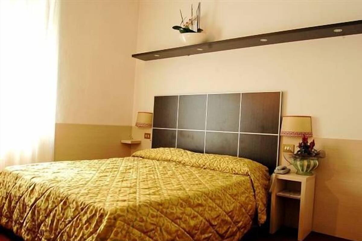 Ein Hotelzimmer mit einem großen Bett, einem Nachttisch, einem Wandregal und einem Beistelltisch mit Lampe.
