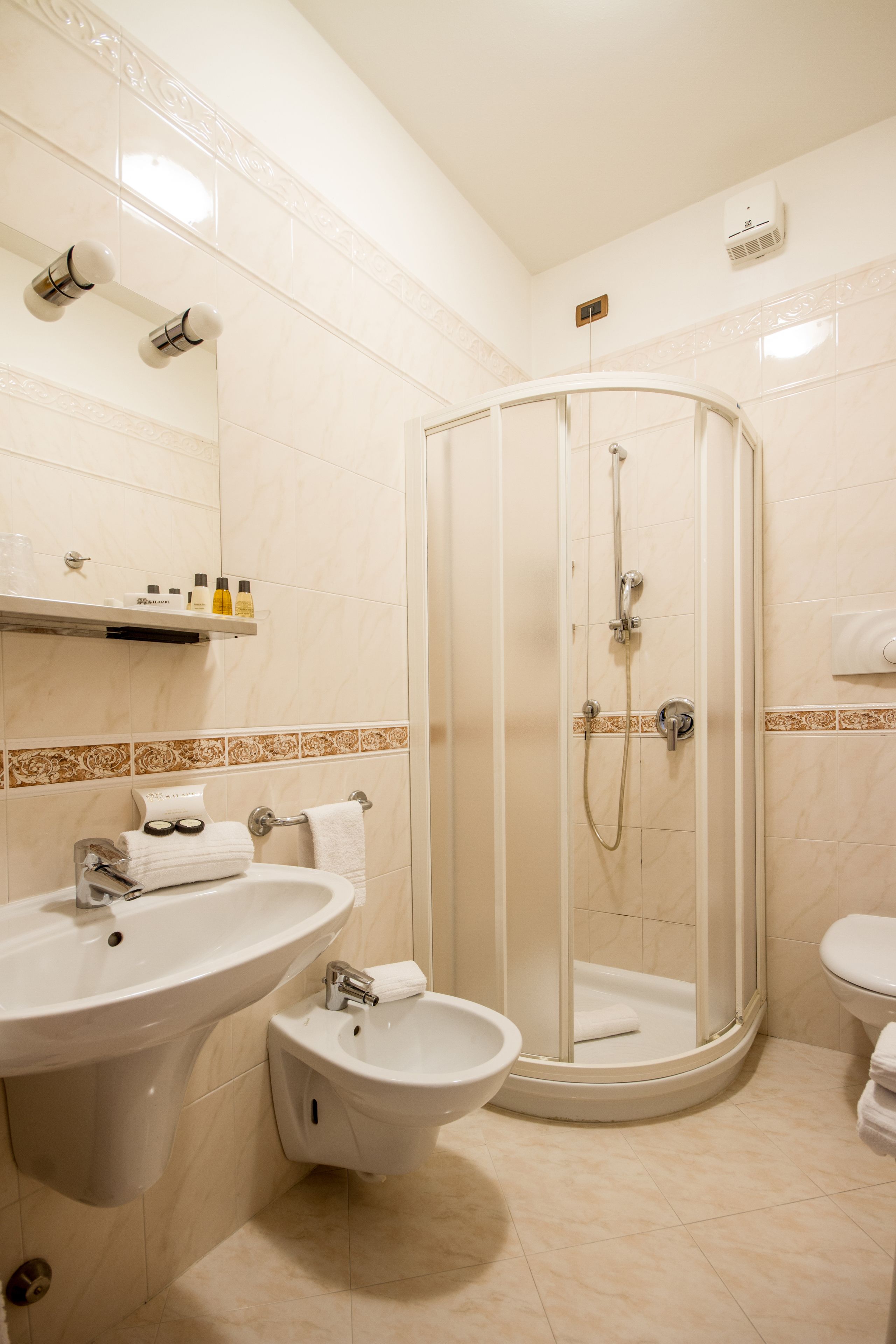 A bathroom with a shower, sink, bidet, and a towel rack.