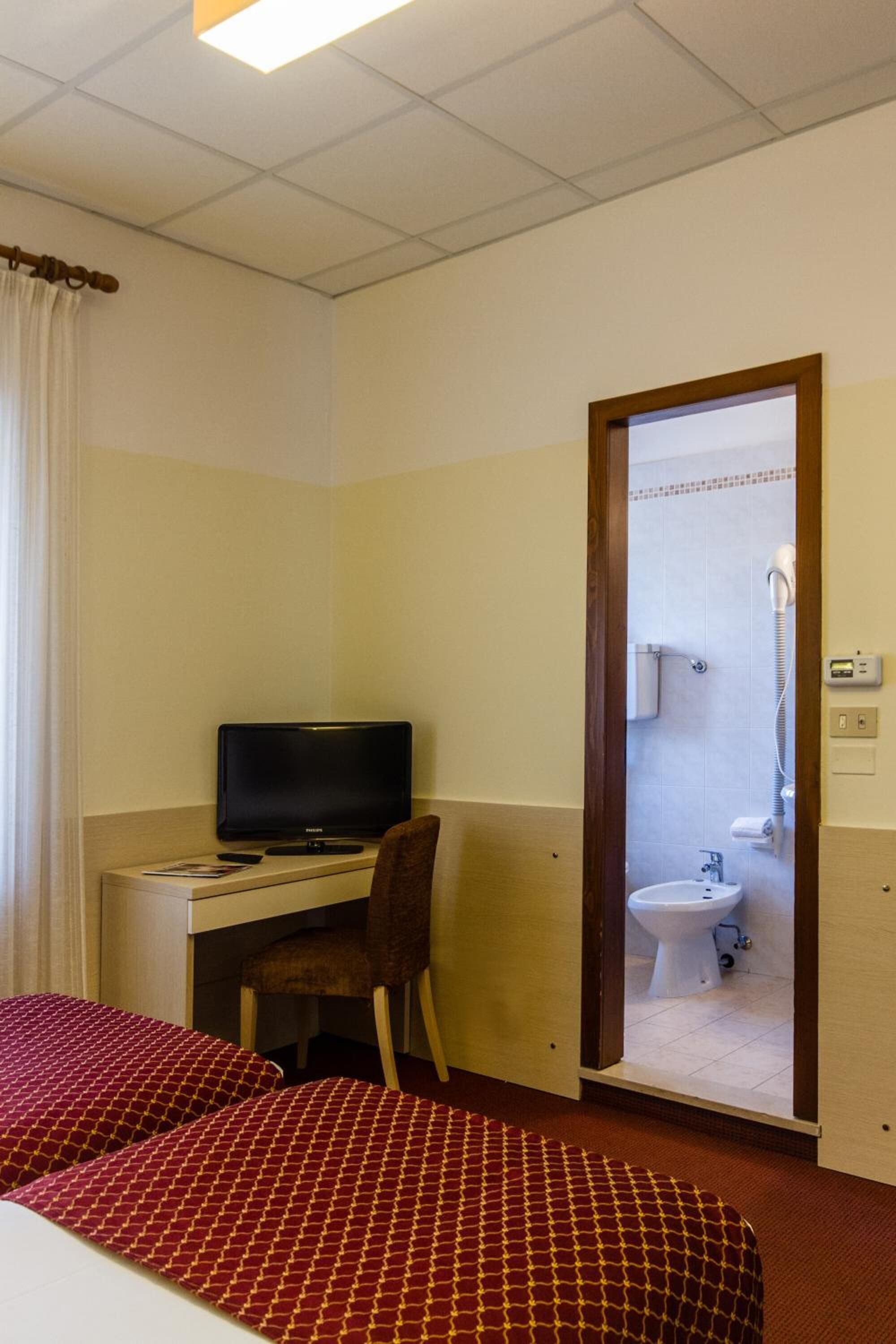 A hotel room with a bed, a desk with a television, a chair, and a bathroom visible through an open door.