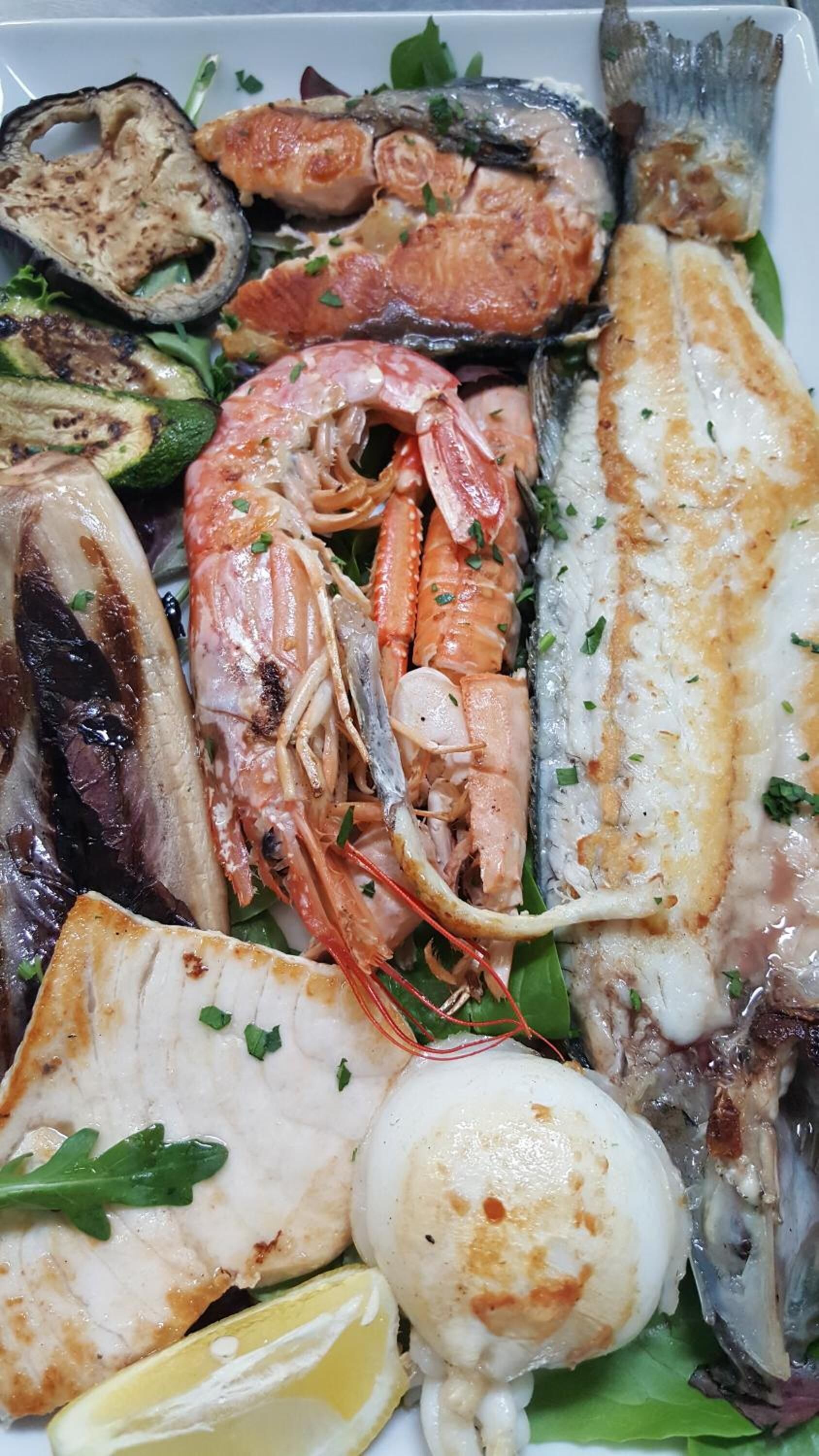 Eine Auswahl an Meeresfrüchten, darunter Garnelen, Fisch und Tintenfisch, serviert auf einer Platte mit Zitronenspalten und Salat.
