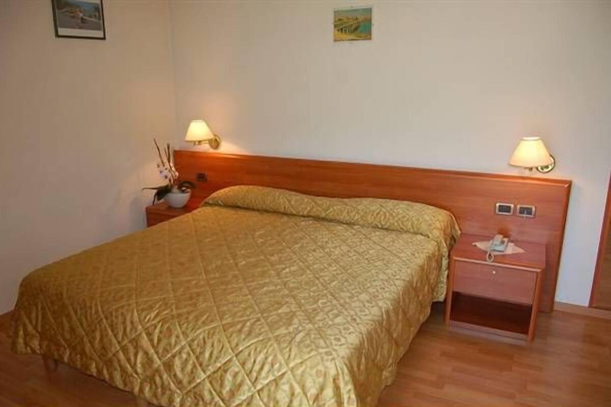 Ein Einzelbett mit gestepptem Kopfteil, zwei Nachttischlampen und ein Nachttisch mit Lampe und einer kleinen Dekoration.
