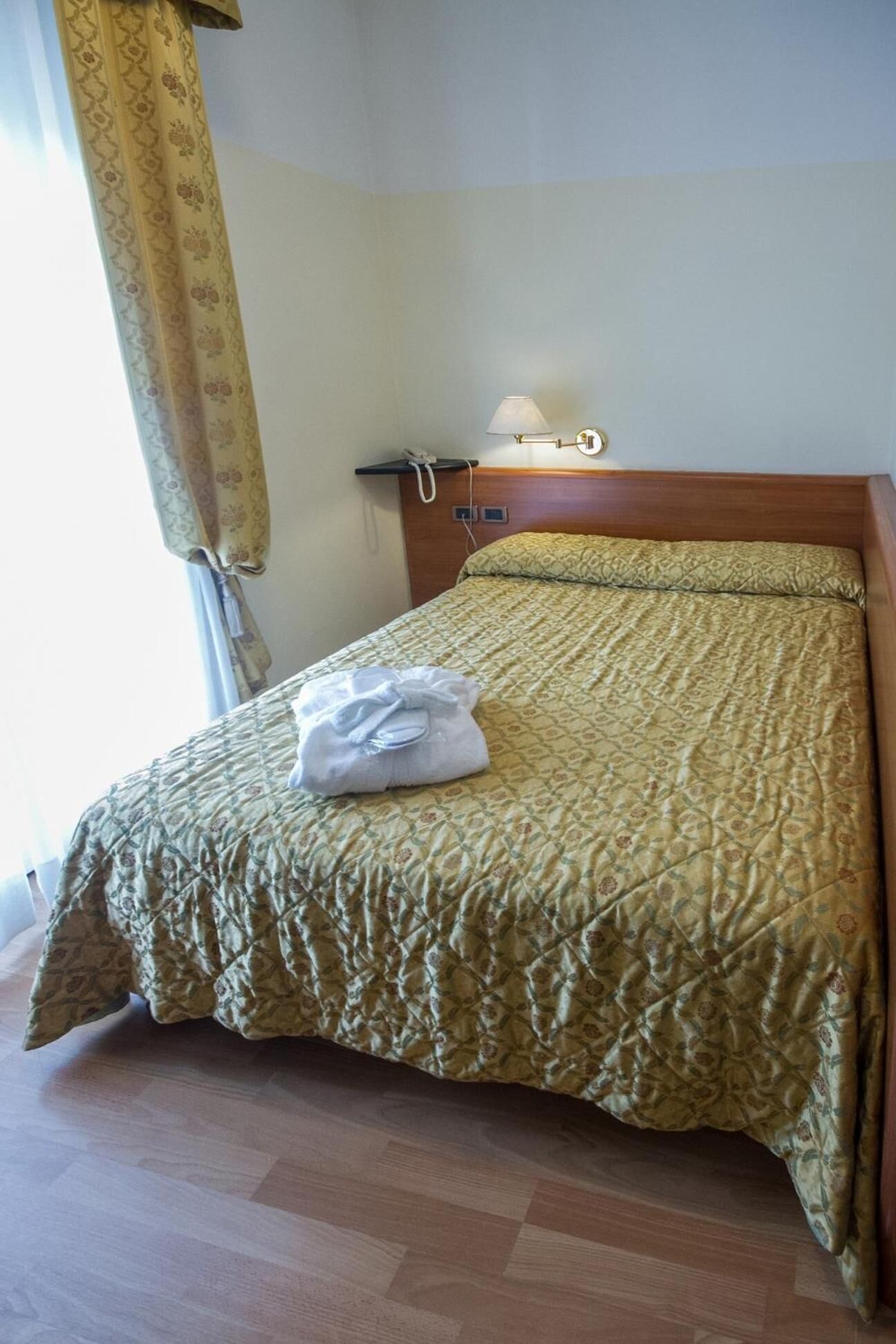 Una habitación de hotel con cama, lámpara de noche, teléfono y una toalla doblada sobre la cama.