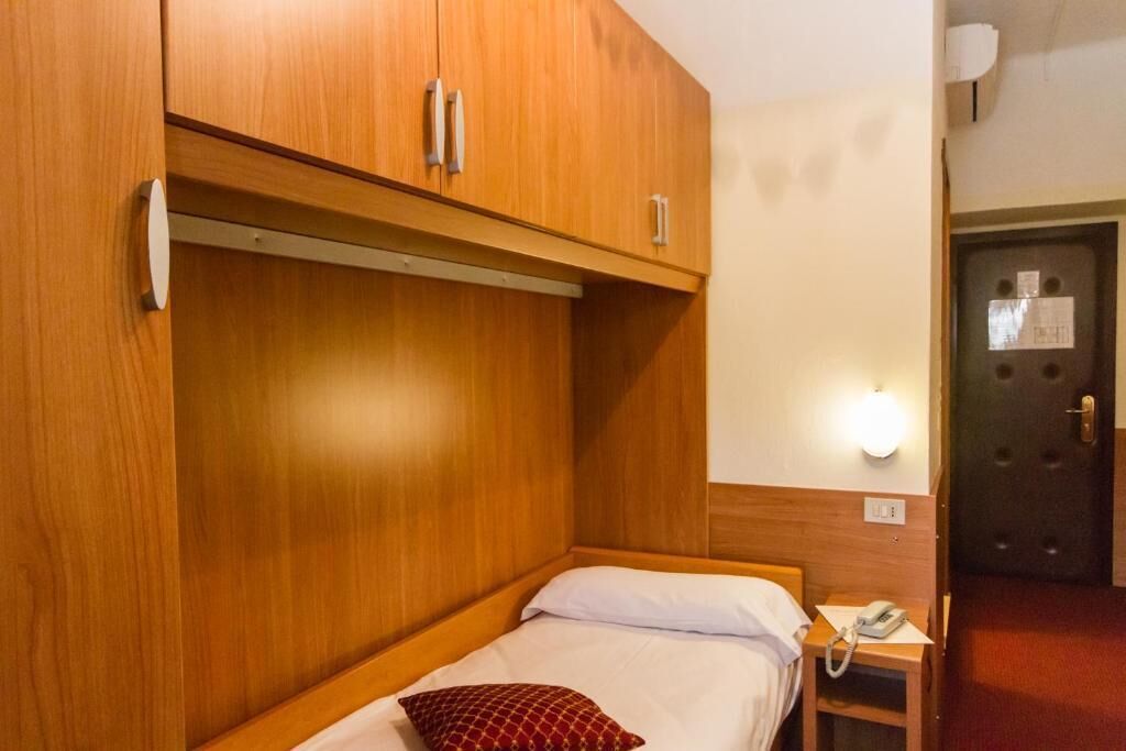 A small, single-bed room with wooden cabinetry and a bedside table with a telephone.