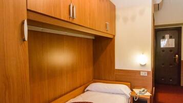 A small, single-bed room with wooden cabinetry and a bedside table with a telephone.