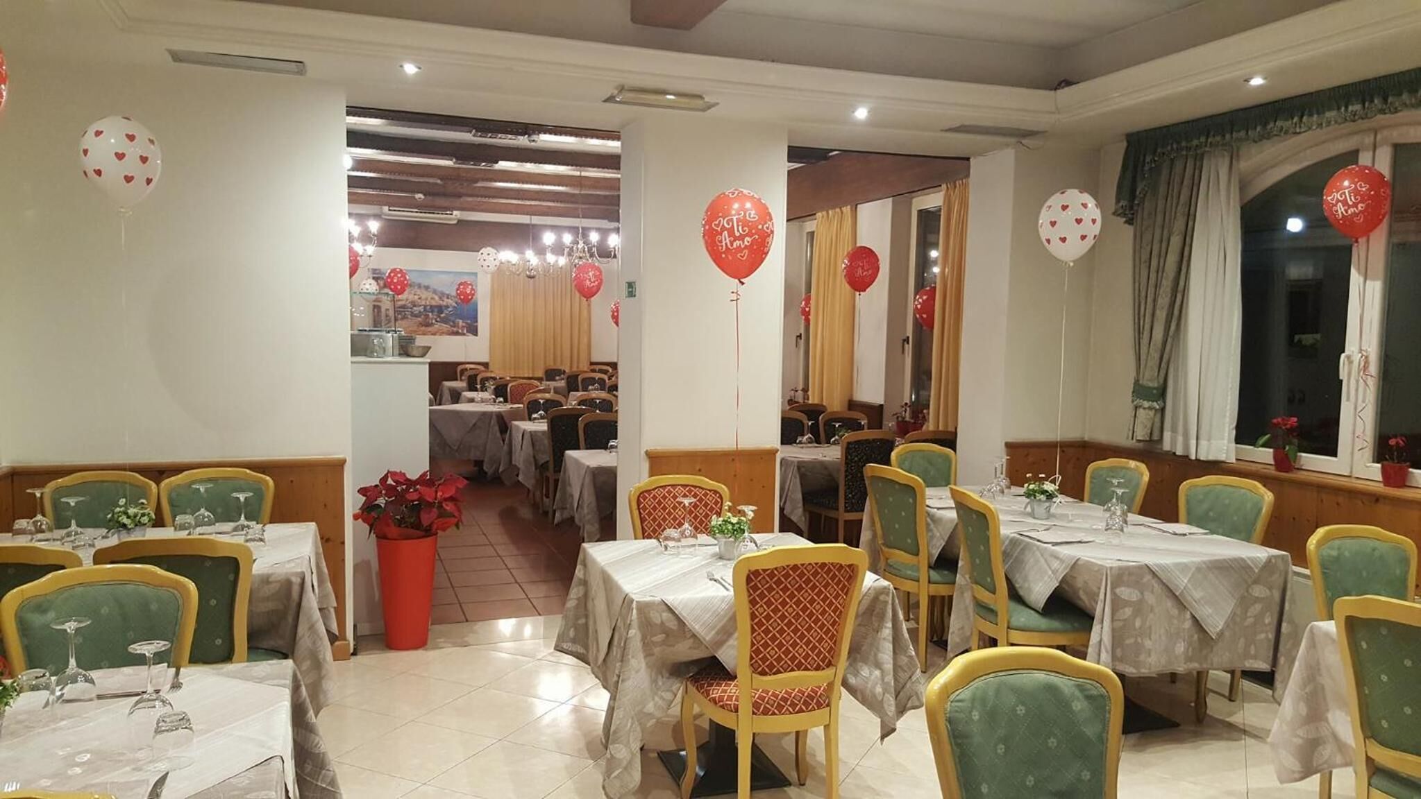 Un restaurante con varias mesas y sillas, globos rojos y una planta en maceta.