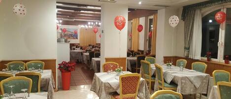 Un restaurante con varias mesas y sillas, globos rojos y una planta en maceta.