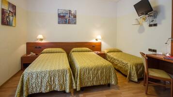 A room with three single beds, a desk with a chair, a TV mounted on the wall, and two bedside lamps.