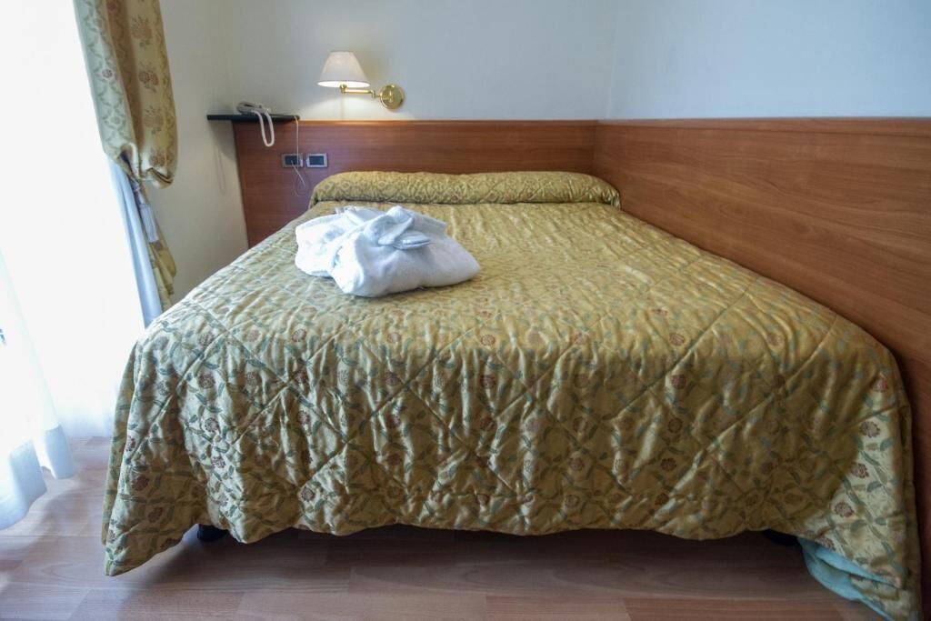 Et hotelværelse med en seng, et natbord, en lampe og et vindue med gardiner.
