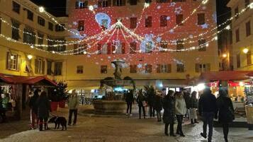 A public square with a fountain, surrounded by buildings with festive lights and decorations.