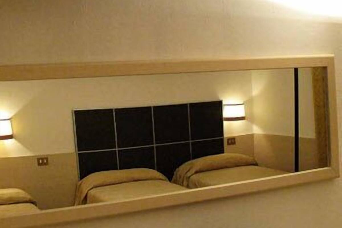 Ein Hotelzimmer mit einem großen Spiegel, einem Bettgestell mit Rasteroptik und zwei Nachttischen mit Lampen.