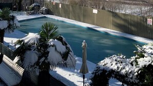 Een zwembad met uitzicht op bergen en een omheind gebied met besneeuwde planten.