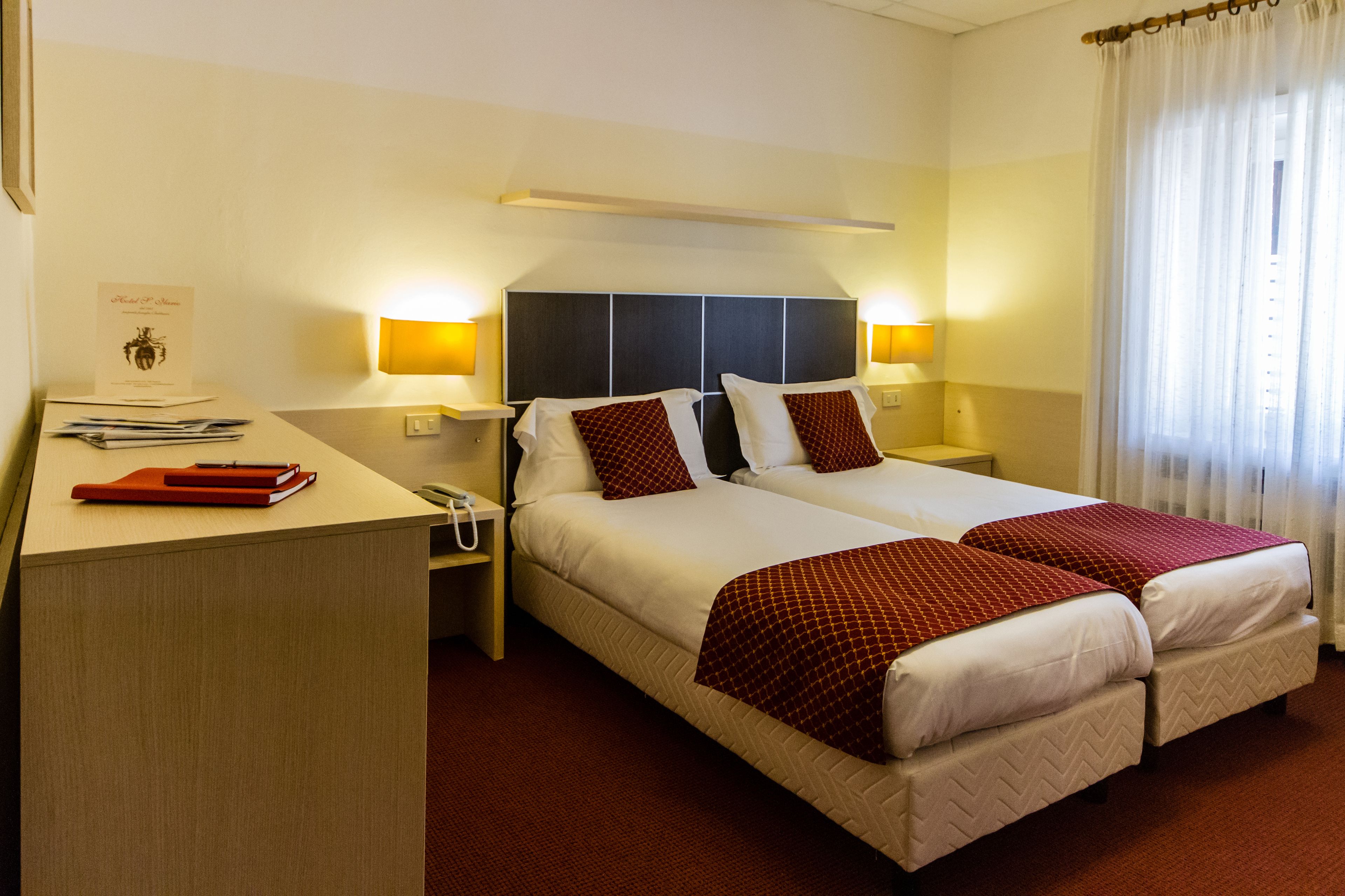 A hotel room with two beds, a desk, and a nightstand.