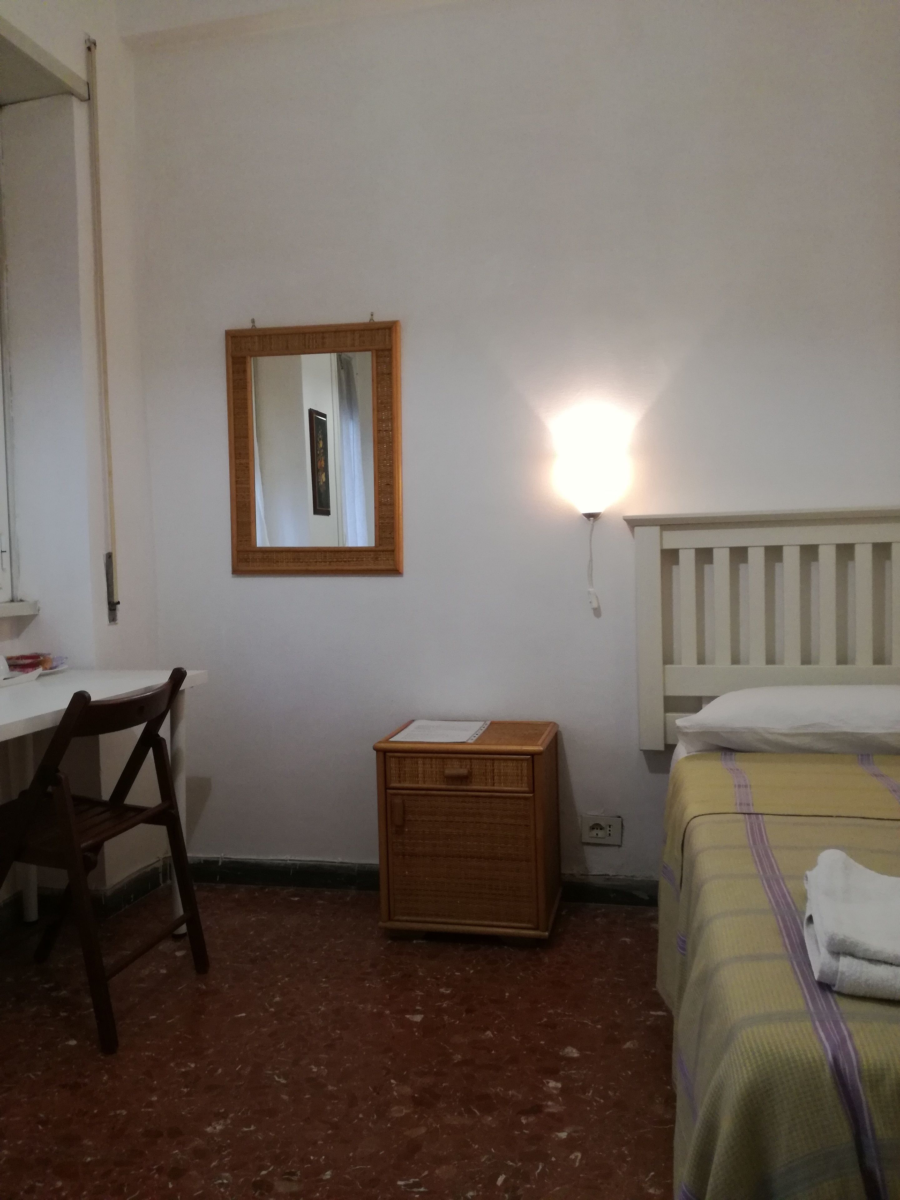 A small, simple room with a desk, chair, bedside table, and a bed.