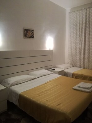 A hotel room with two beds, a nightstand, a bedside table, a wall-mounted lamp, and a window with curtains. - B&B Gioacchino Testa (Rome)