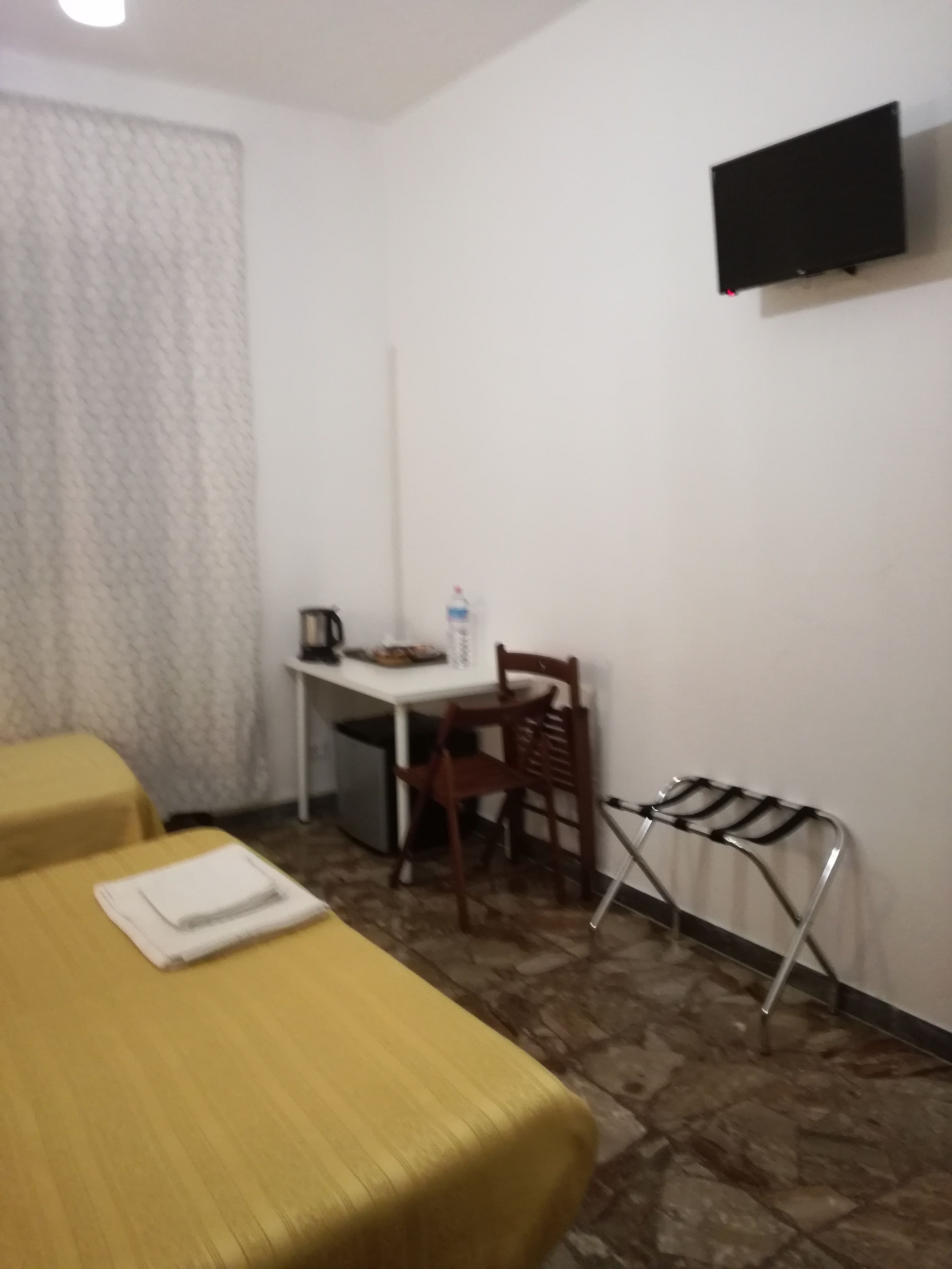 Habitación de hotel con dos camas, un escritorio, una silla, un televisor montado en la pared y una mesita con una botella de agua.