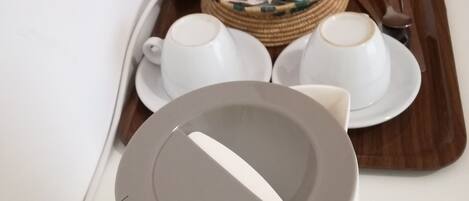 A coffee maker, two white cups, a tray with tea bags, and a spoon on a table.