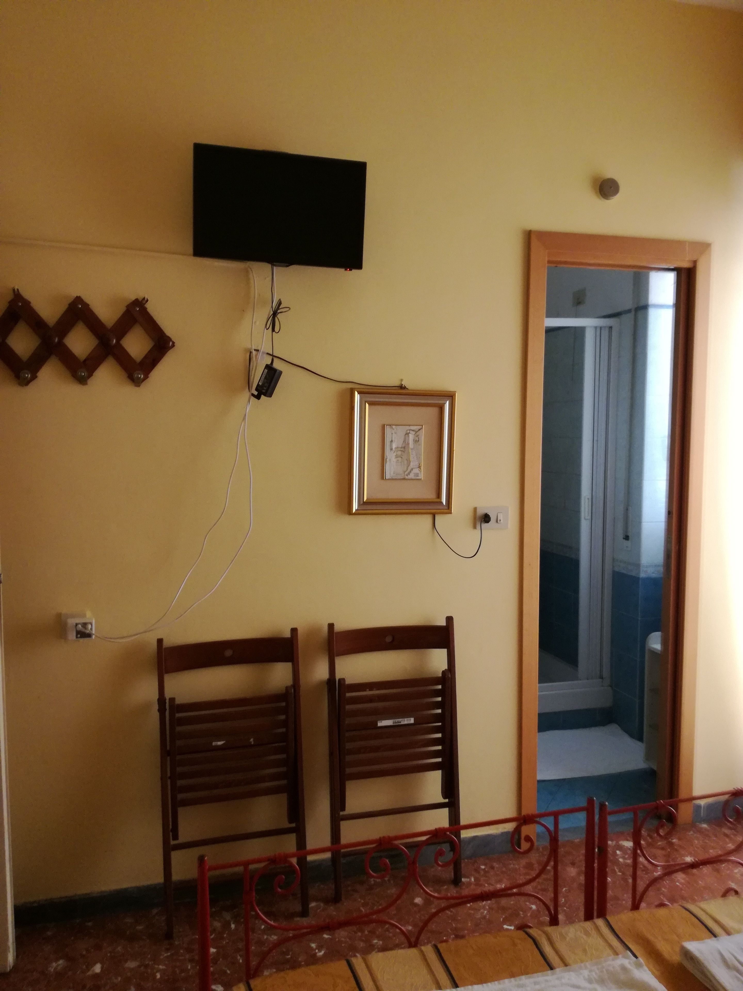 A room with two wooden chairs, a television mounted on the wall, and a framed picture.