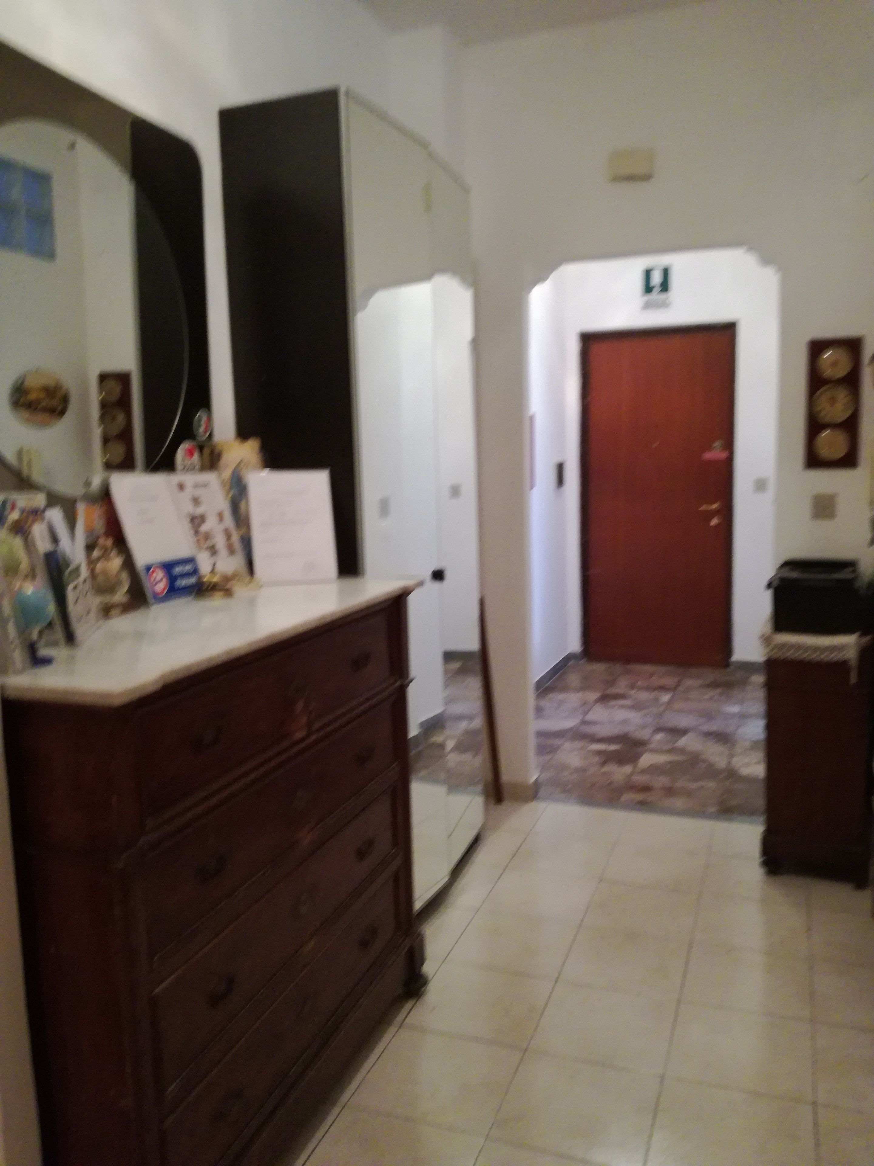 A room with a wooden dresser, a white refrigerator, a tiled floor, and a door with a sign above it.