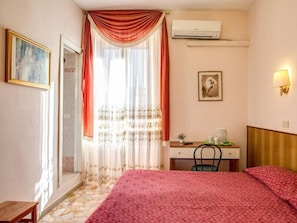 A hotel room with a bed, a desk, a chair, an air conditioner, and a painting on the wall. - B&B Giovy Rome (Rome)