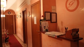 Un hall d’accueil d’hôtel avec un tapis rouge, des portes en bois et un comptoir de réception agrémenté d’une carte et de certificats encadrés.