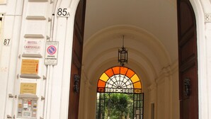 Une entrée en arc de cercle, sur laquelle on peut lire une enseigne indiquant « Hôtel Campidoglio » et un panneau « Stationnement interdit ».