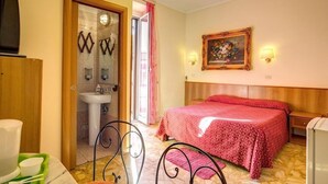 Une chambre à coucher avec un lit, une table de chevet, un téléviseur fixé au mur, un tableau, et une salle de bain visible à travers une porte ouverte.