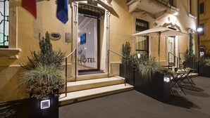 Entrada de hotel con un letrero, escalones y mesas al aire libre.
