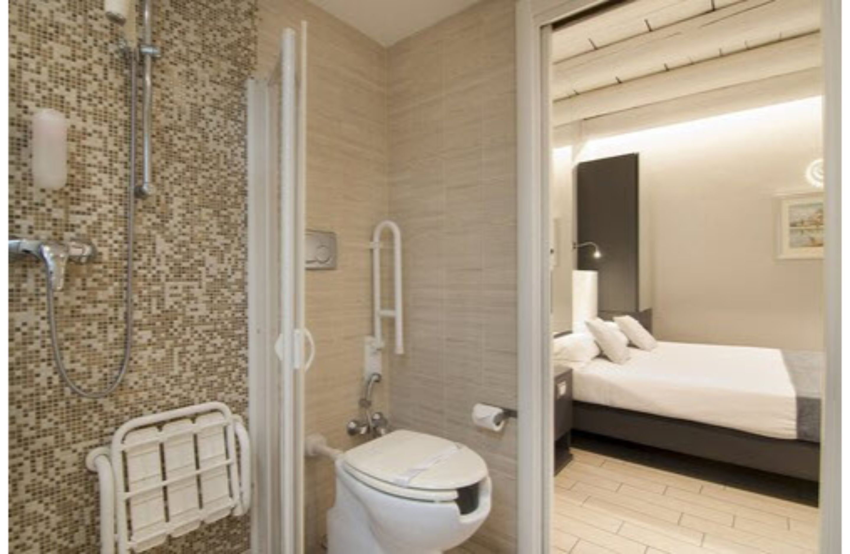 Ein Badezimmer mit Dusche und WC, sowie ein Bett im angrenzenden Raum.