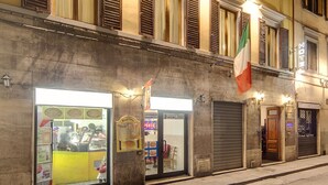 A hotel facade with multiple windows, a flag, and a storefront with a bright interior. - Hotel Camilla Guelfa (Florence)