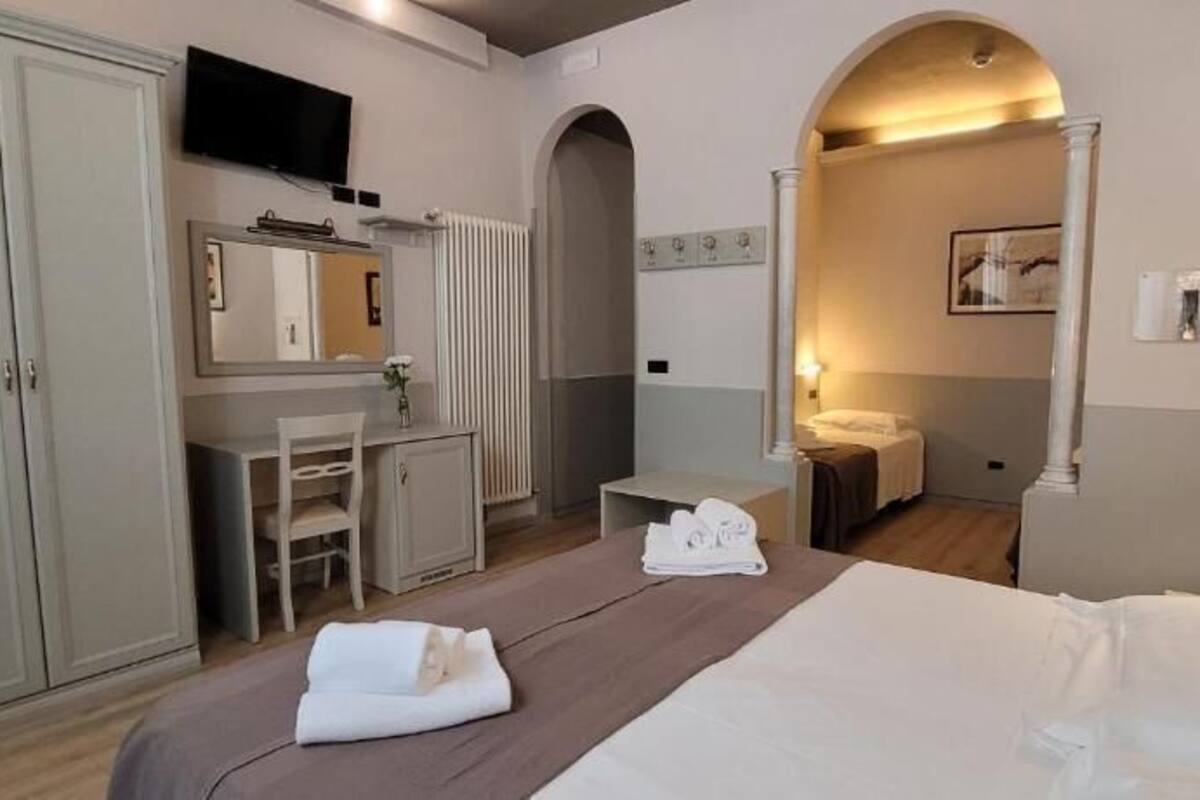 Habitación de hotel con cama, escritorio, silla, televisión y baño visible a través de un arco.