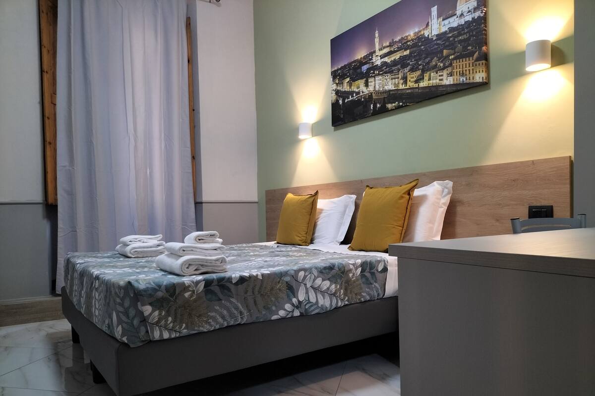 Una cama bien hecha con toallas dobladas, un cabecero con dos almohadas y una mesita de noche con una lámpara.