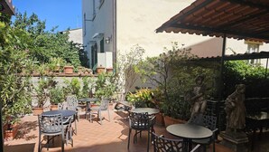 An outdoor patio area with terracotta-tiled flooring, metal chairs, and tables. There are potted plants and a statue of a woman. - Hotel Camilla Guelfa (Florence)