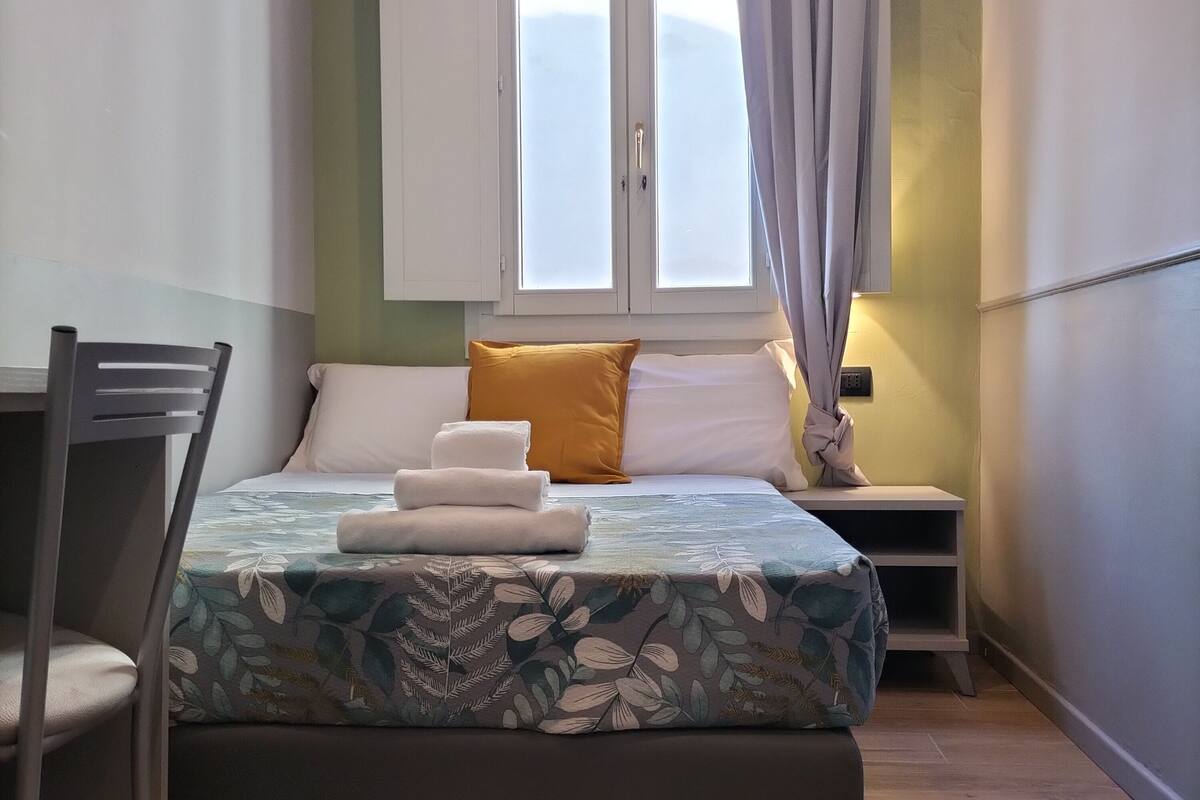 Un dormitorio con cama, una silla, una mesita de noche y un equipo de aire acondicionado.