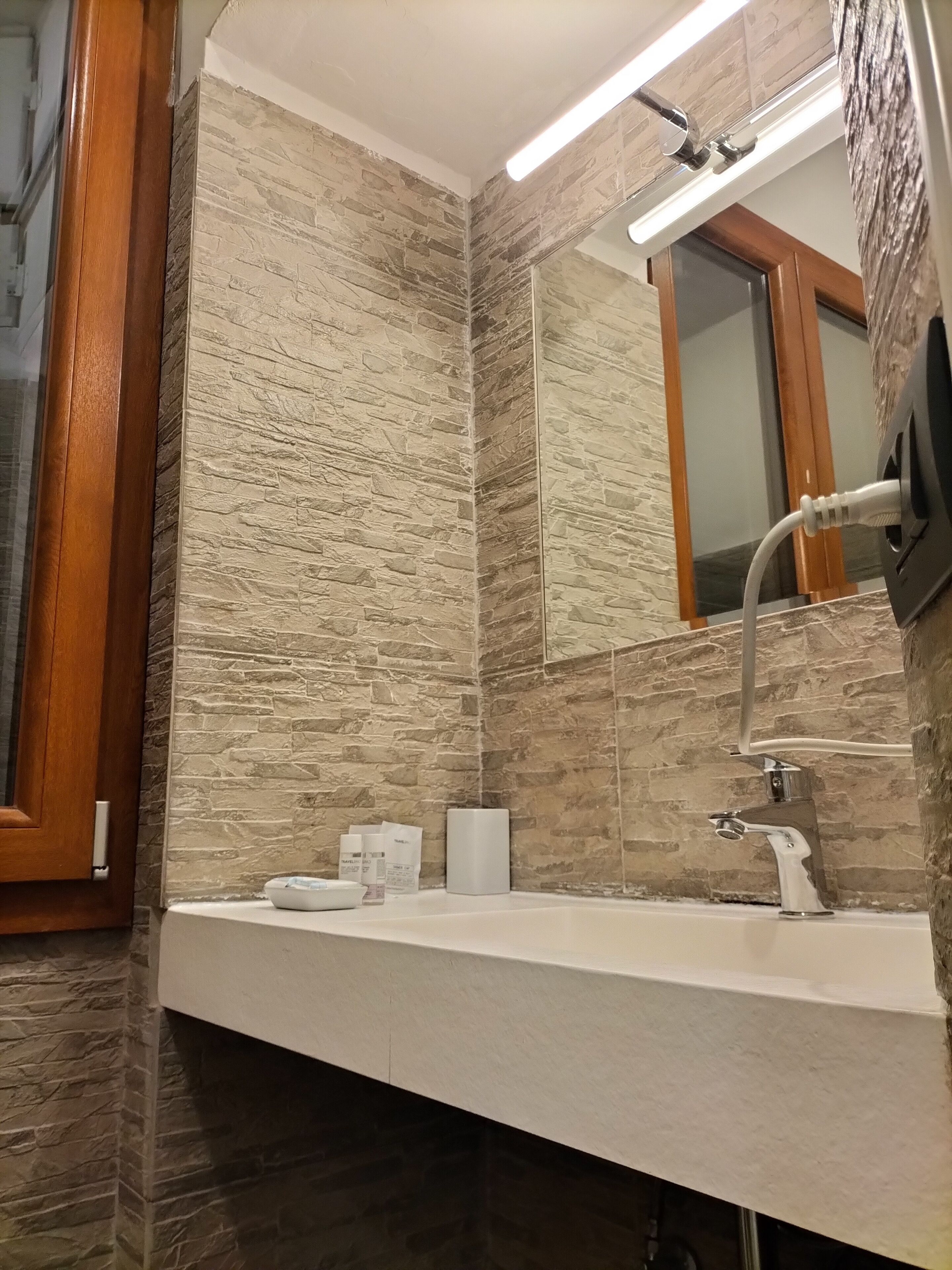 Een badkamer met een wand met een stenen textuur, een moderne wastafel en een spiegel.