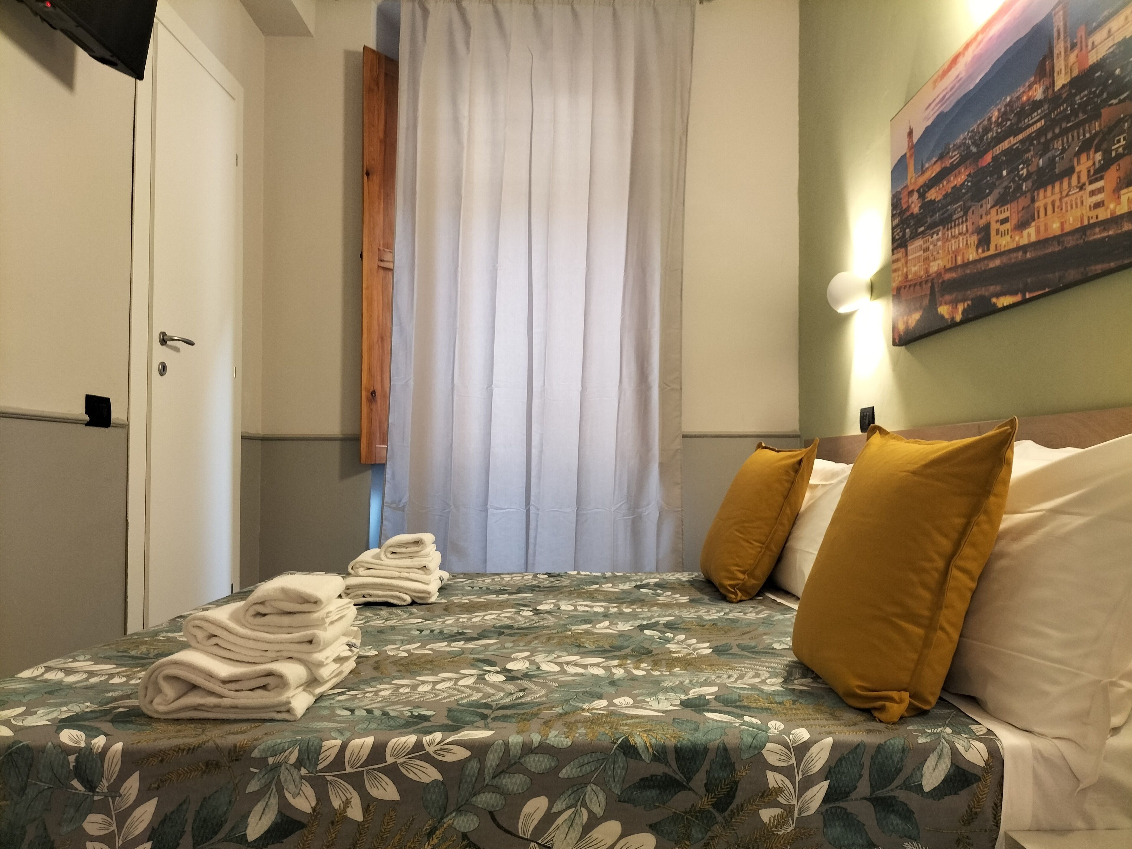 A hotel room with a bed, a door, a curtain, and a painting on the wall.